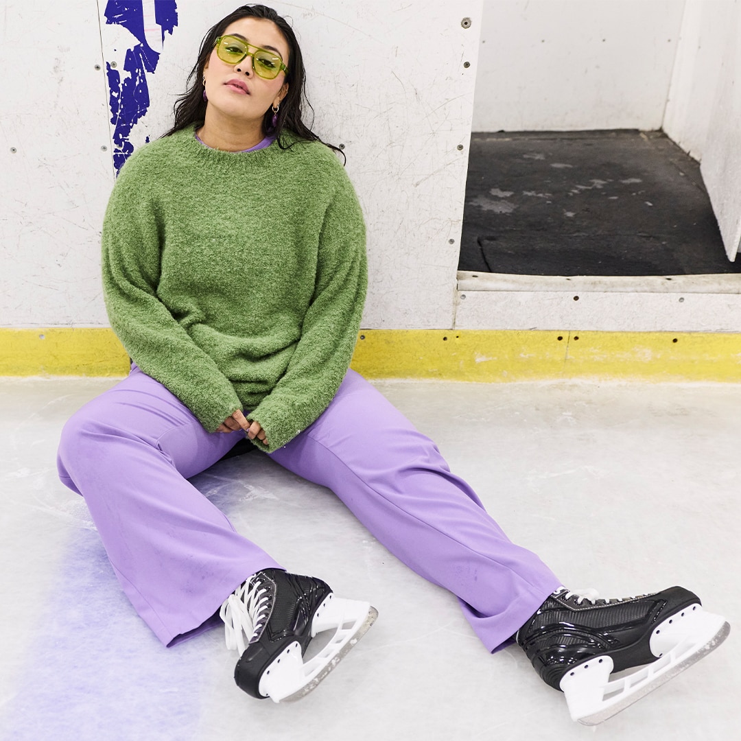 The model is wearing a green woollen jumper and purple trousers.