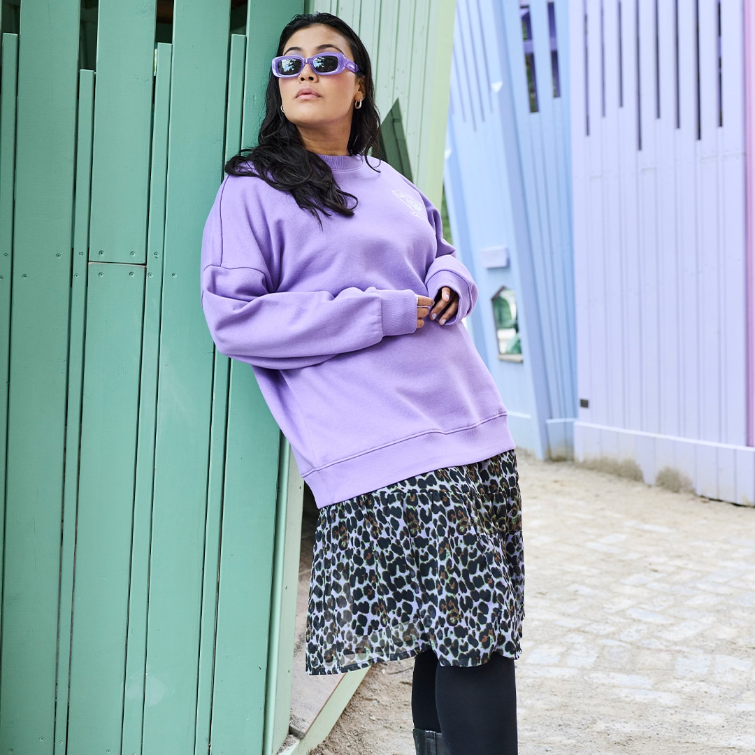 The model is wearing a purple sweater and a short black patterned skirt.