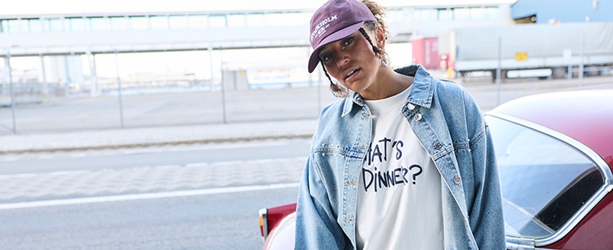 The model is wearing a purple and green striped blouse and matching tight-fitting purple trousers.