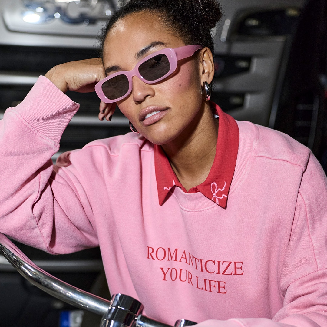 The model is standing on the ice wearing ice skates and a green and purple checked coat.