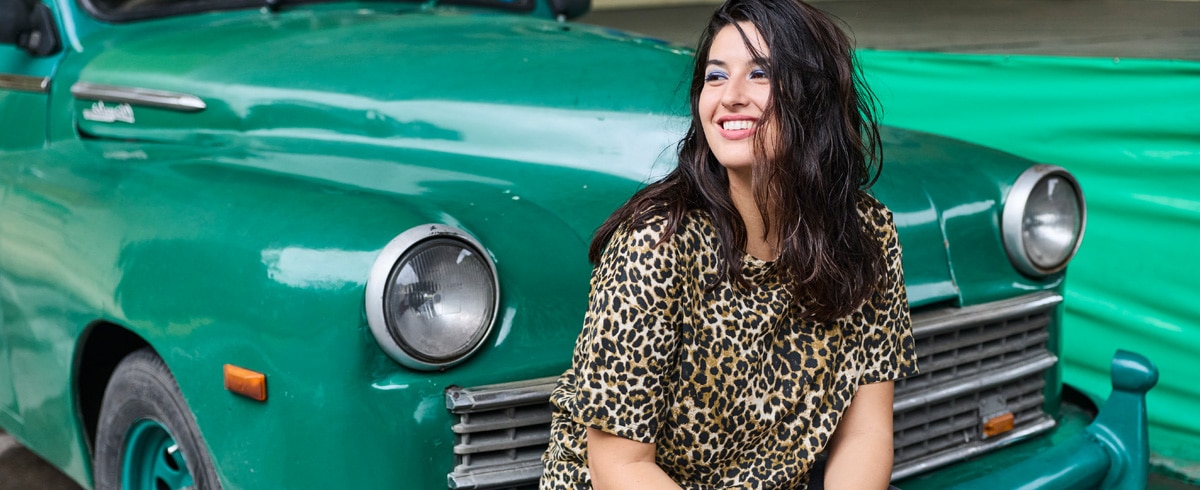 The model is wearing a purple and green striped blouse and matching tight-fitting purple trousers.