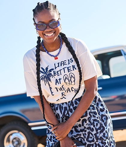 The model is wearing a white T-shirt with black lettering and purple and black trousers with a leopard-print design