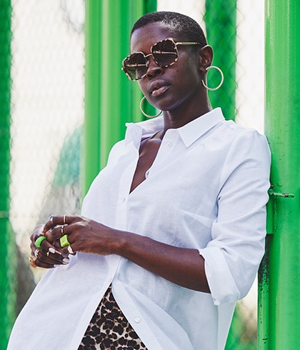 Dark-skinned woman with short hair, sunglasses and a white blouse.