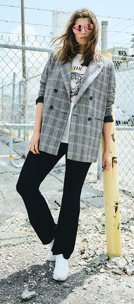 Model posing in front of a fence with sunglasses and a plaid blazer