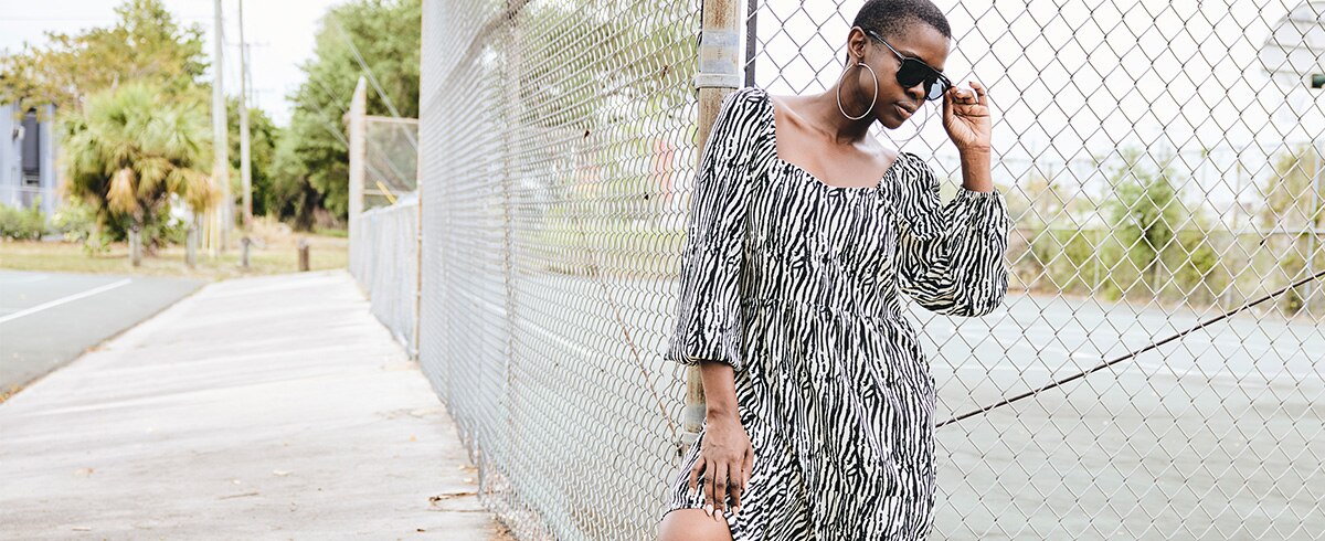 Dark-skinned model is posing in front of a fence wearing a dress with stripes