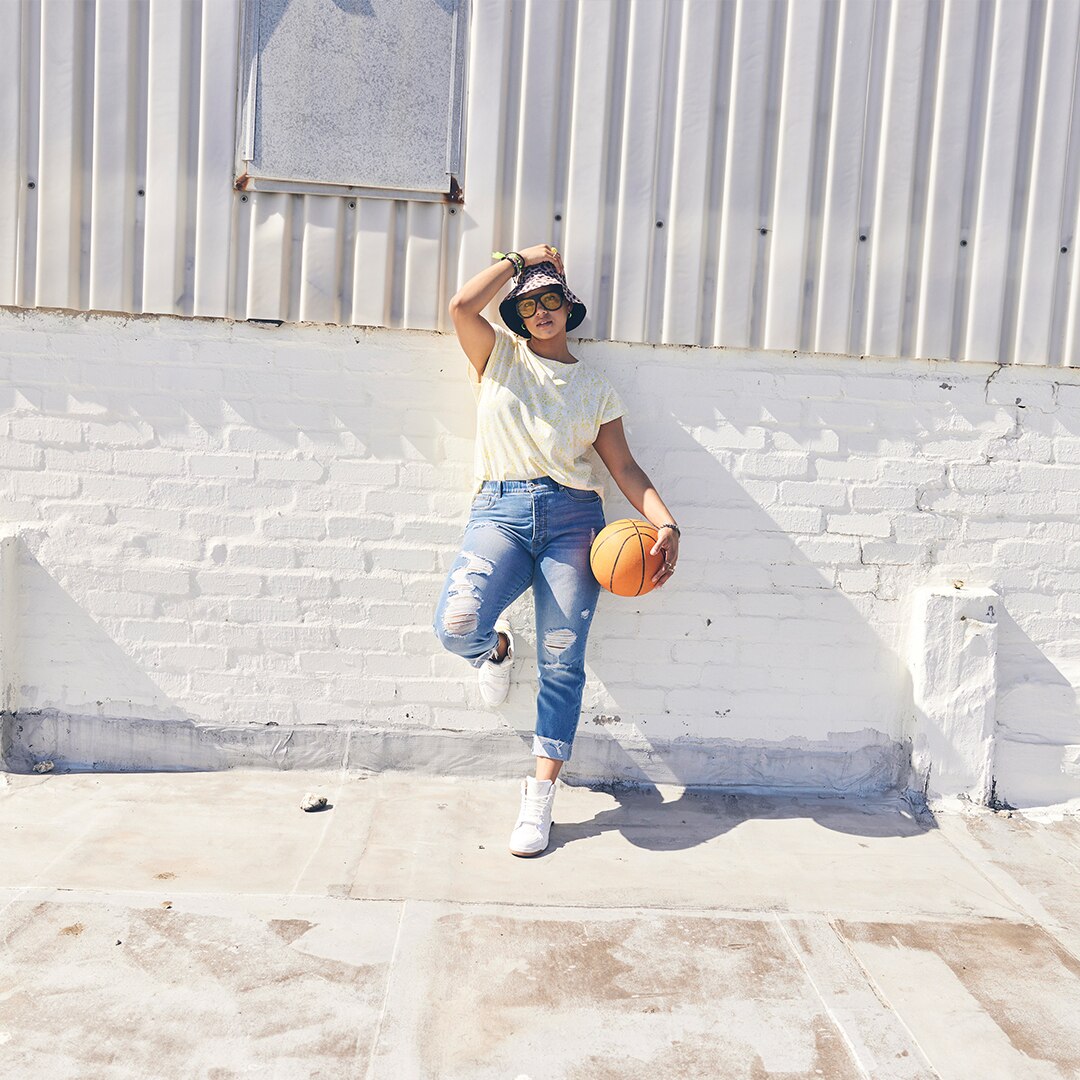 Young woman with sunglasses leaning against a wall while holding a baskett ball. 