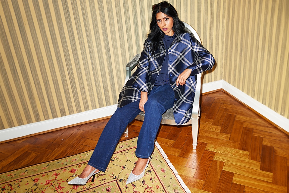 The model poses in the studio and wears a blue and white striped blouse with an additional floral print with her jeans