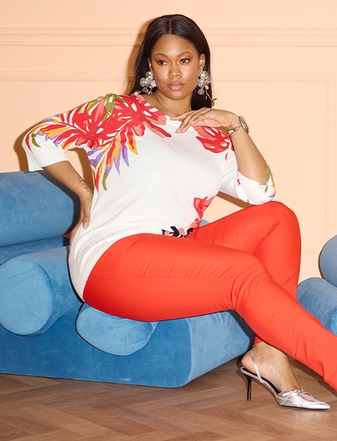 The model poses in red trousers and a colourful blouse