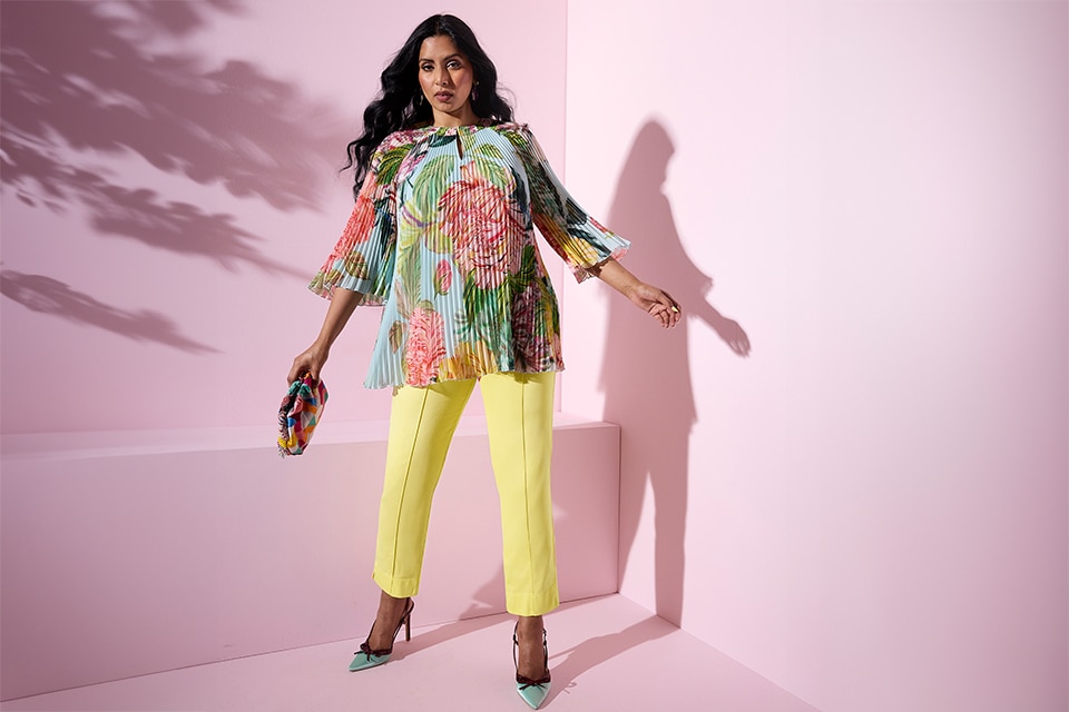 The model wears a floral blouse and yellow pants.
