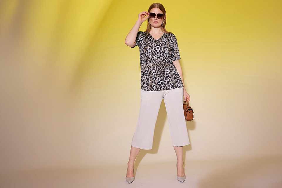 The model wears white pants and a leopard printed t-shirt.