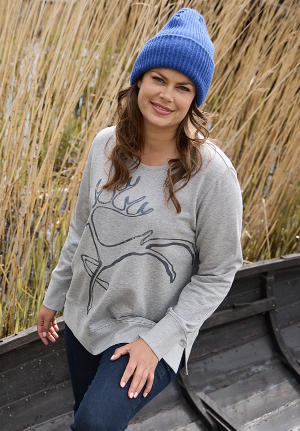 Model trägt eine Jeansjacke und sitzt auf einem Felsen