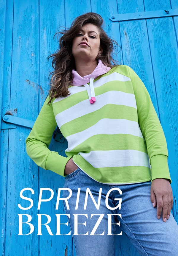 Model trägt eine Jeansjacke und sitzt auf einem Felsen