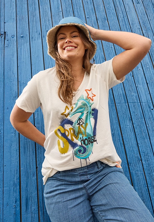 Model trägt eine Jeansjacke und sitzt auf einem Felsen