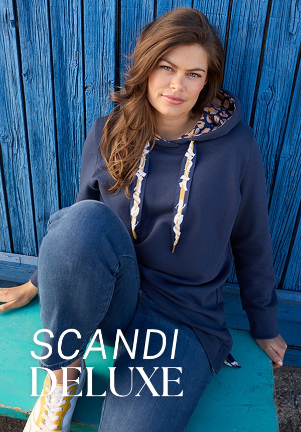 Model trägt eine Jeansjacke und sitzt auf einem Felsen