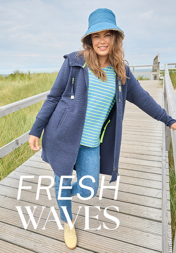 Model trägt eine Jeansjacke und sitzt auf einem Felsen