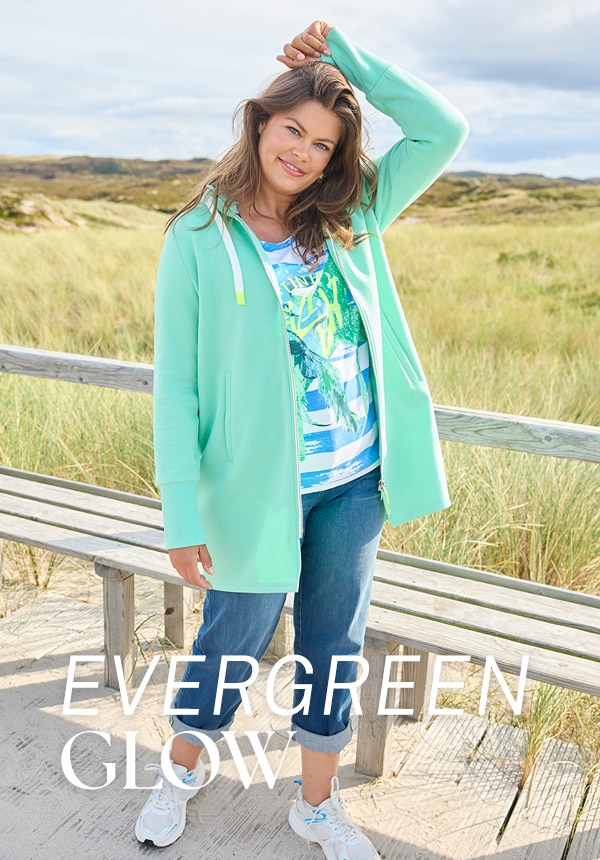 Model trägt eine Jeansjacke und sitzt auf einem Felsen