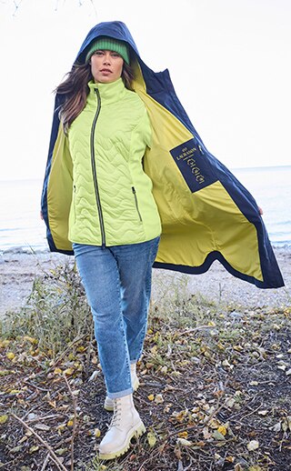 Eine Frau läuft am Strand und trägt eine gelbe Steppjacke