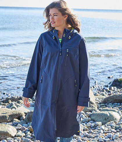 Eine Frau mit langem blauen Rgenmantel läuft am Strand.