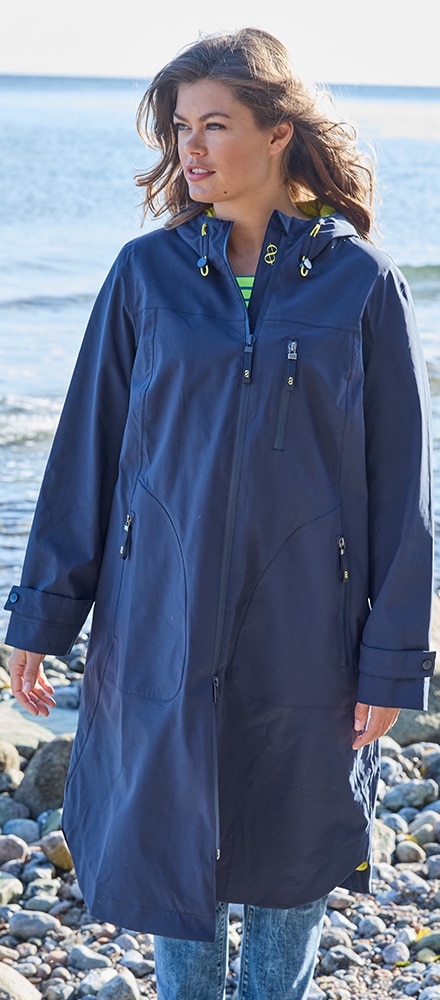 Eine Frau mit langem blauen Rgenmantel läuft am Strand.