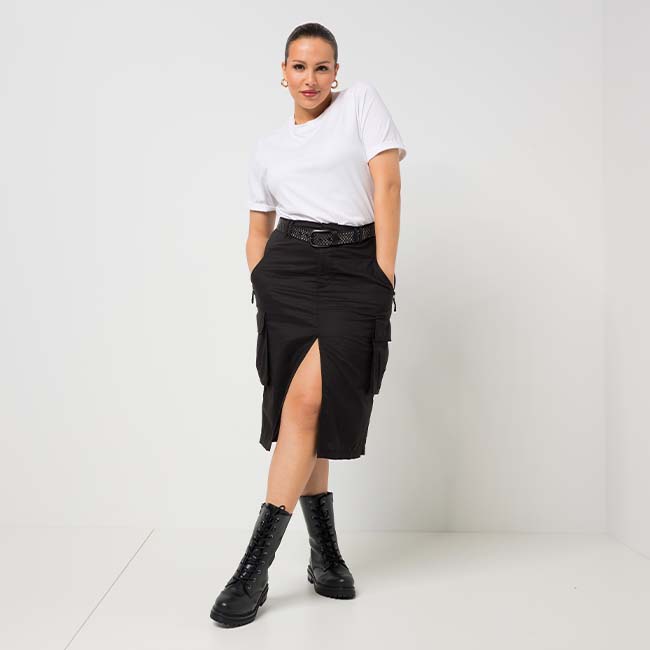 The model wears a black cargo skirt and poses in front of a white studio background