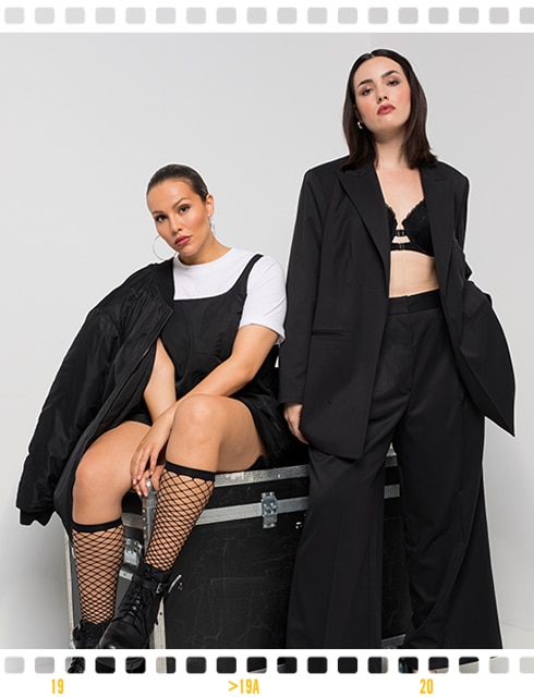 Two models pose sitting on a box in front of a white studio background