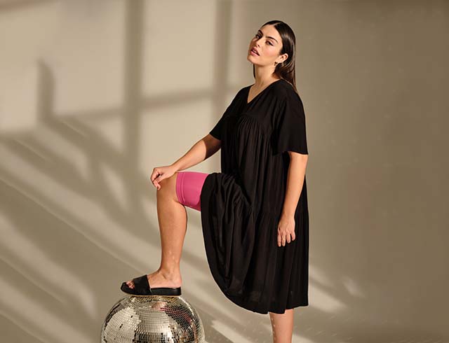 The model poses in a black dress and pink pants