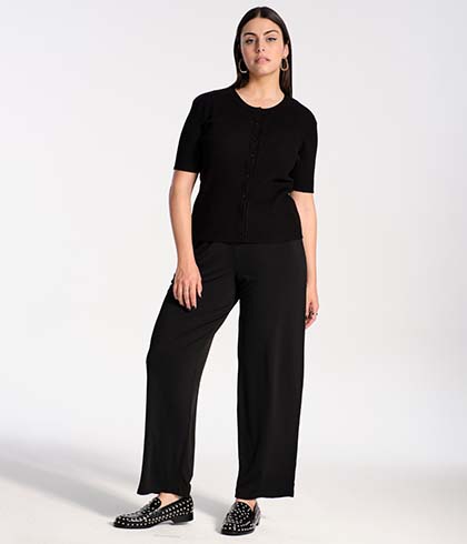 Model is posing in a black knit shirt and relaxed jersey pants 