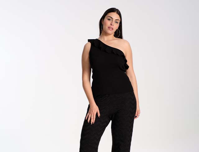 Model poses in a black one shoulder knit top