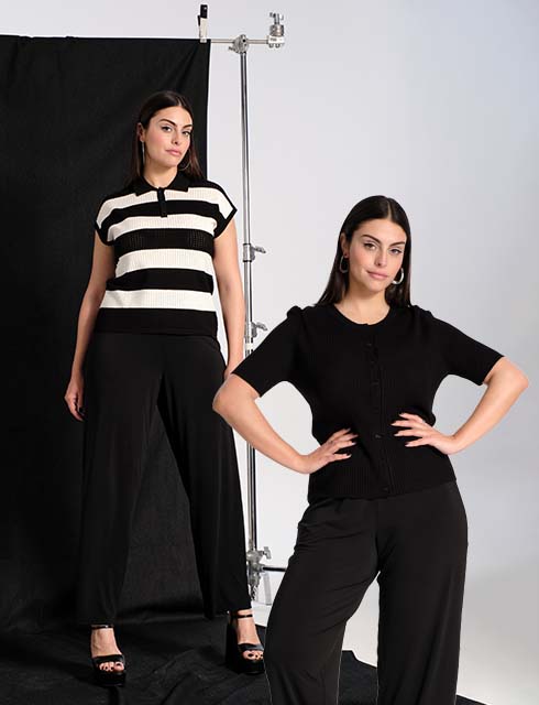 The model stands  in front of a studio-setup wearing a black and white  pullunder and a black pants