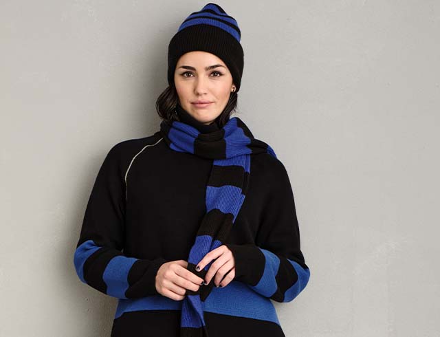the model wears a black and blue striped scarf and a matching cap
