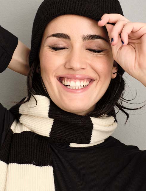 the model wears a cap and laughs into the camera 