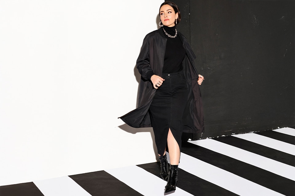 The model poses in a black skirt and a black coat