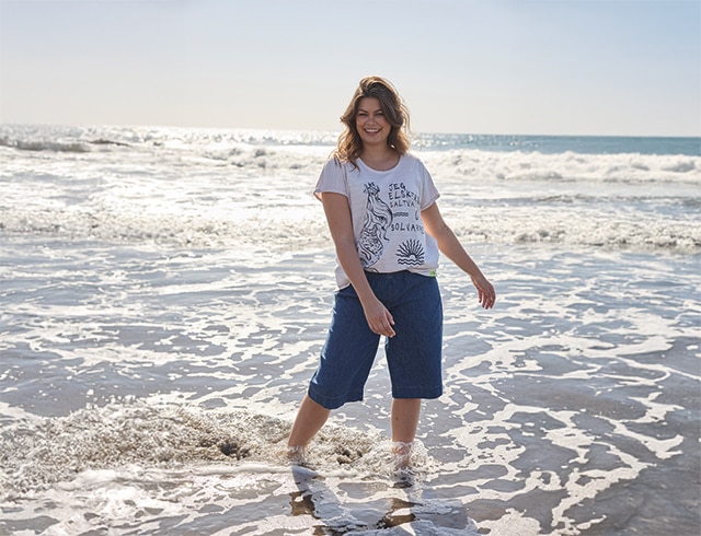 The model wears a white shirt with print and blue Bermuda shorts