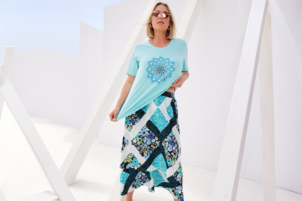 The model is wearing a patterned skirt with a blue shirt
