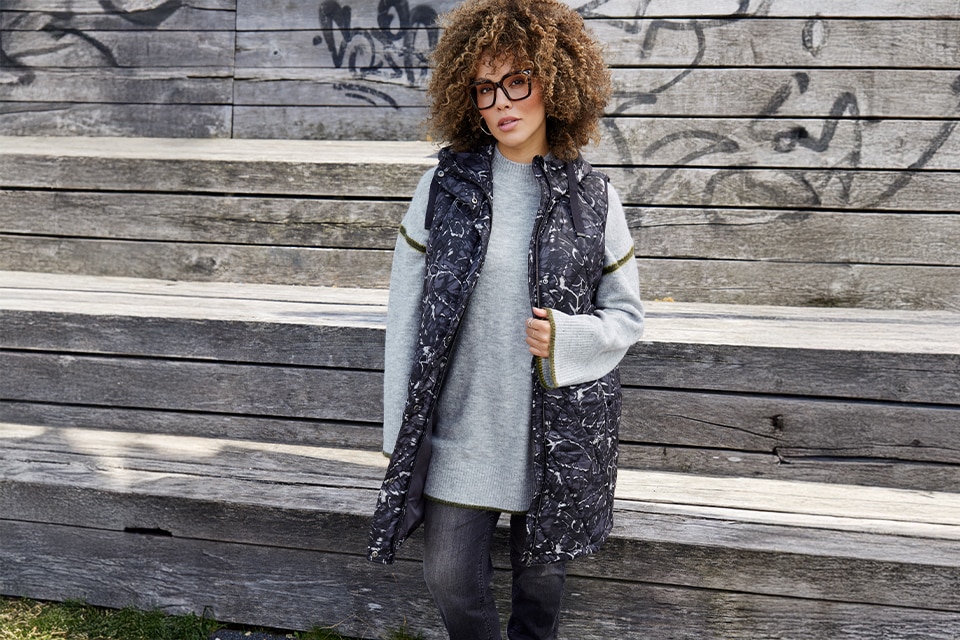 The model is wearing a grey sweater with a long Vest