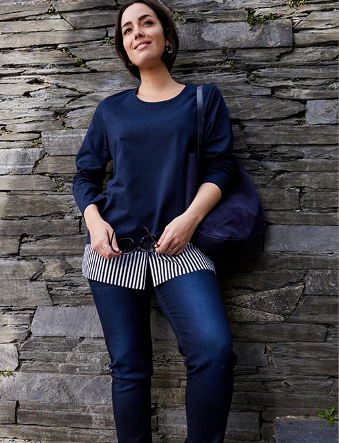 The model is wearing a striped blouse with a blue sweater over it, paired with jeans.