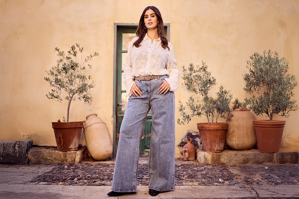 The model wears a white blouse and jeans