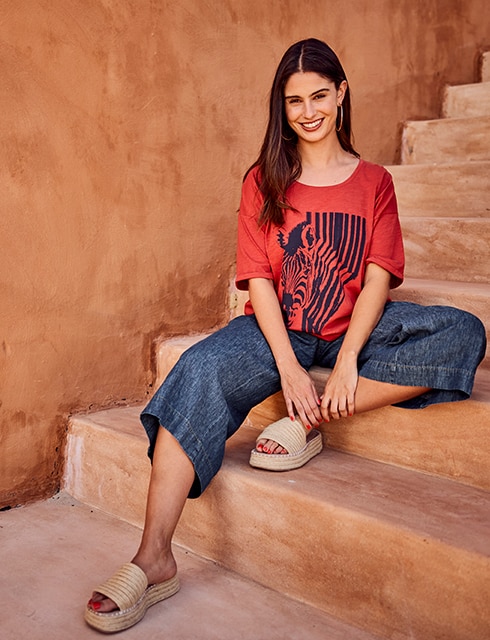 The model is wearing a red t-shirt with print and jeans.