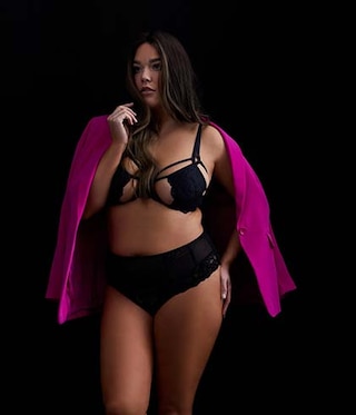 The model poses in a black bra and a pink cardigan 