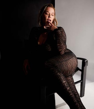 The model wears a catsuits and sits on a chair
