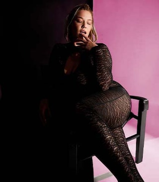 The model wears a catsuits and sits on a chair