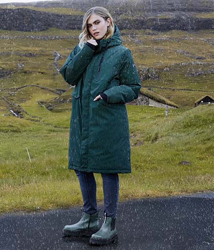 Model with dark green jacket stands in front of green landscape