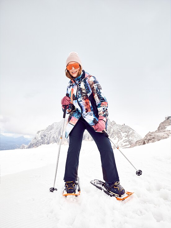 Woman in a colourful jacket and blue trousers skis