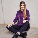 The model is wearing a purple sweater with embellishment
