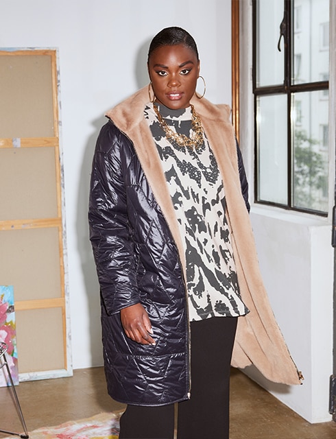 The model poses in a gallery wearing a reversible jacket and a patterned blouse 


