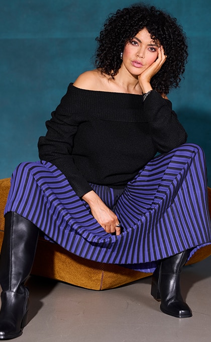 The model poses sitting in a purple suit