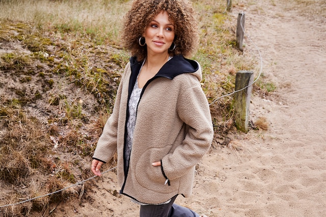 The model wears a beige dress and a coat