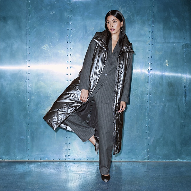 The model poses in a gray pantsuit with stripes and wears a silver vest.