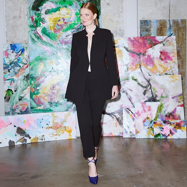 The model wears a blazer around a pair of acetate trousers