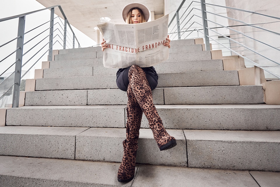 The model poses seated and wears overknees in a leo pattern